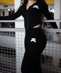 Person wearing a black outfit with white logos standing on a balcony.