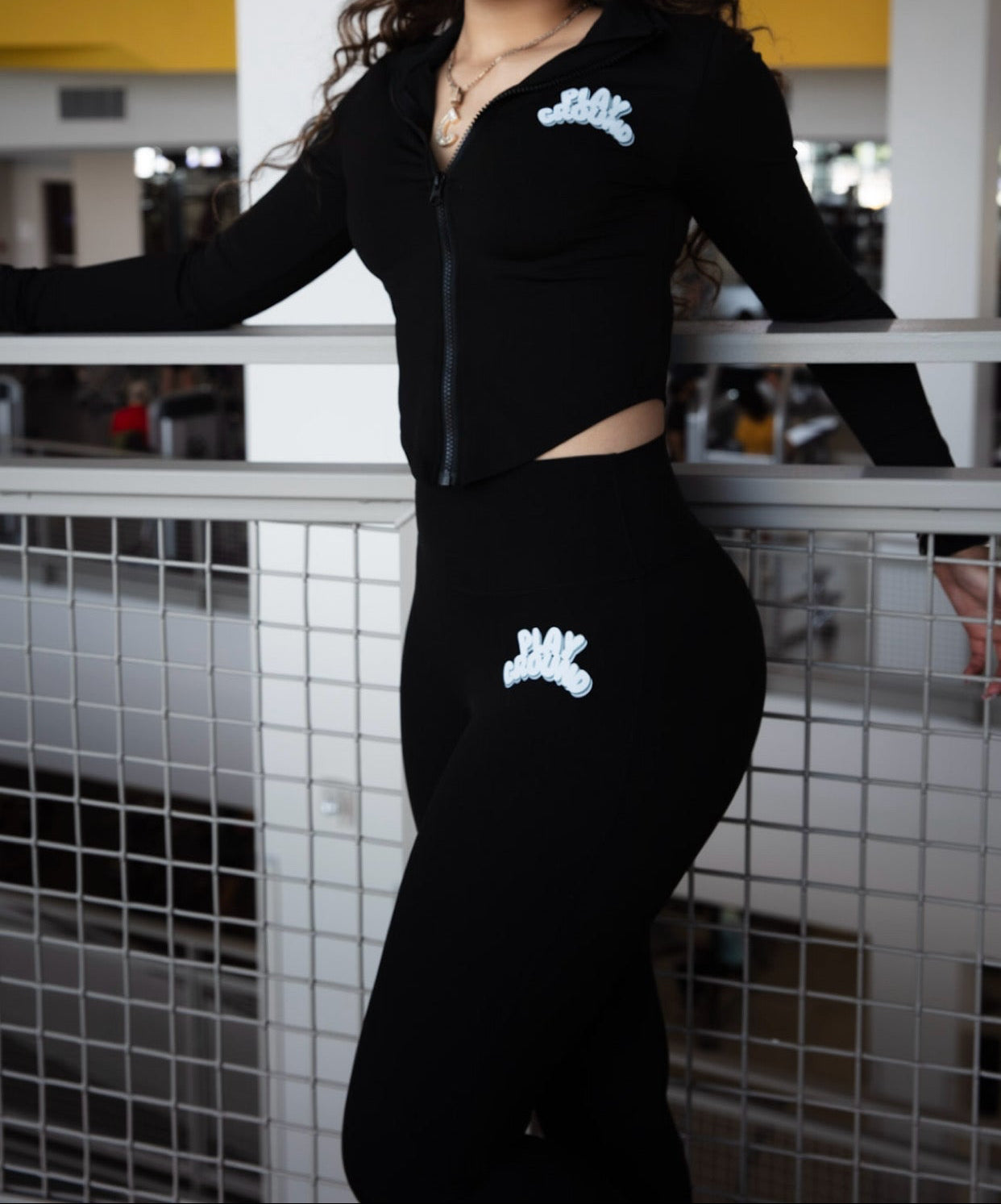 Person wearing a black outfit with white logos standing on a balcony.